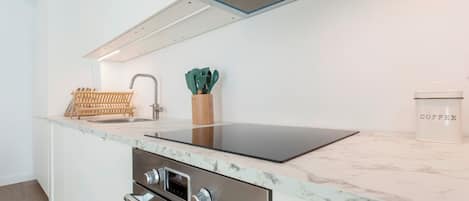 A modern kitchen with a built-in oven, a stainless steel range hood, and a marble countertop.