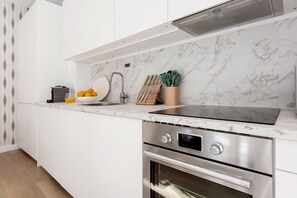 Une cuisine moderne avec des meubles blancs, une cuisinière en acier inoxydable, un four encastré et un dosseret en marbre.