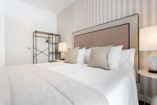 Une chambre d’hôtel moderne avec un grand lit, une table de chevet avec une lampe, une armoire avec un miroir et un mur à rayures.