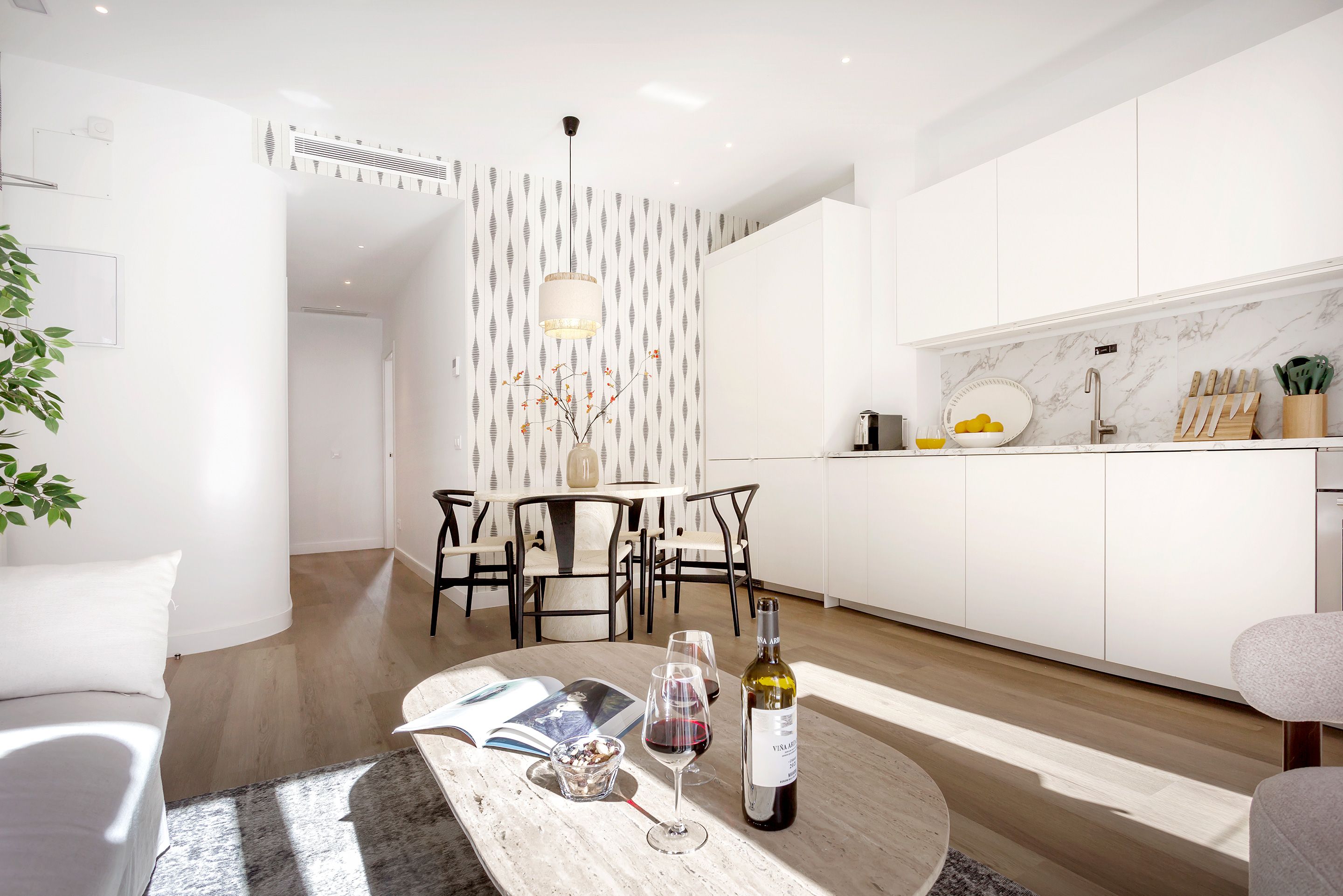 A modern kitchen with white cabinetry, a marble backsplash, and a dining area with a round table and chairs.
