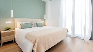 Een moderne slaapkamer met een groot bed, een nachtkastje met een plantje en dunne gordijnen voor het raam.
