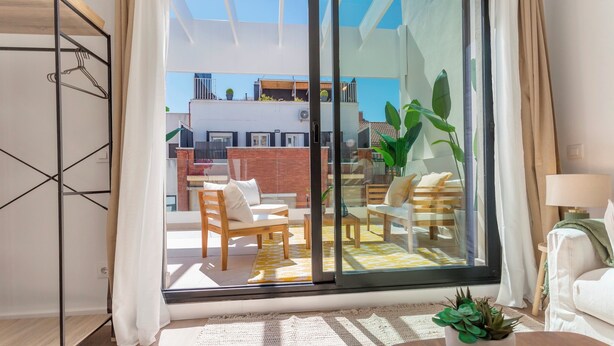 Een moderne woonkamer met een schuifdeur naar een balkon, ingericht met een bank, stoelen en een salontafel.