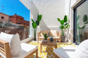 Un balcón con sofá, dos sillas, una mesita y plantas en macetas.