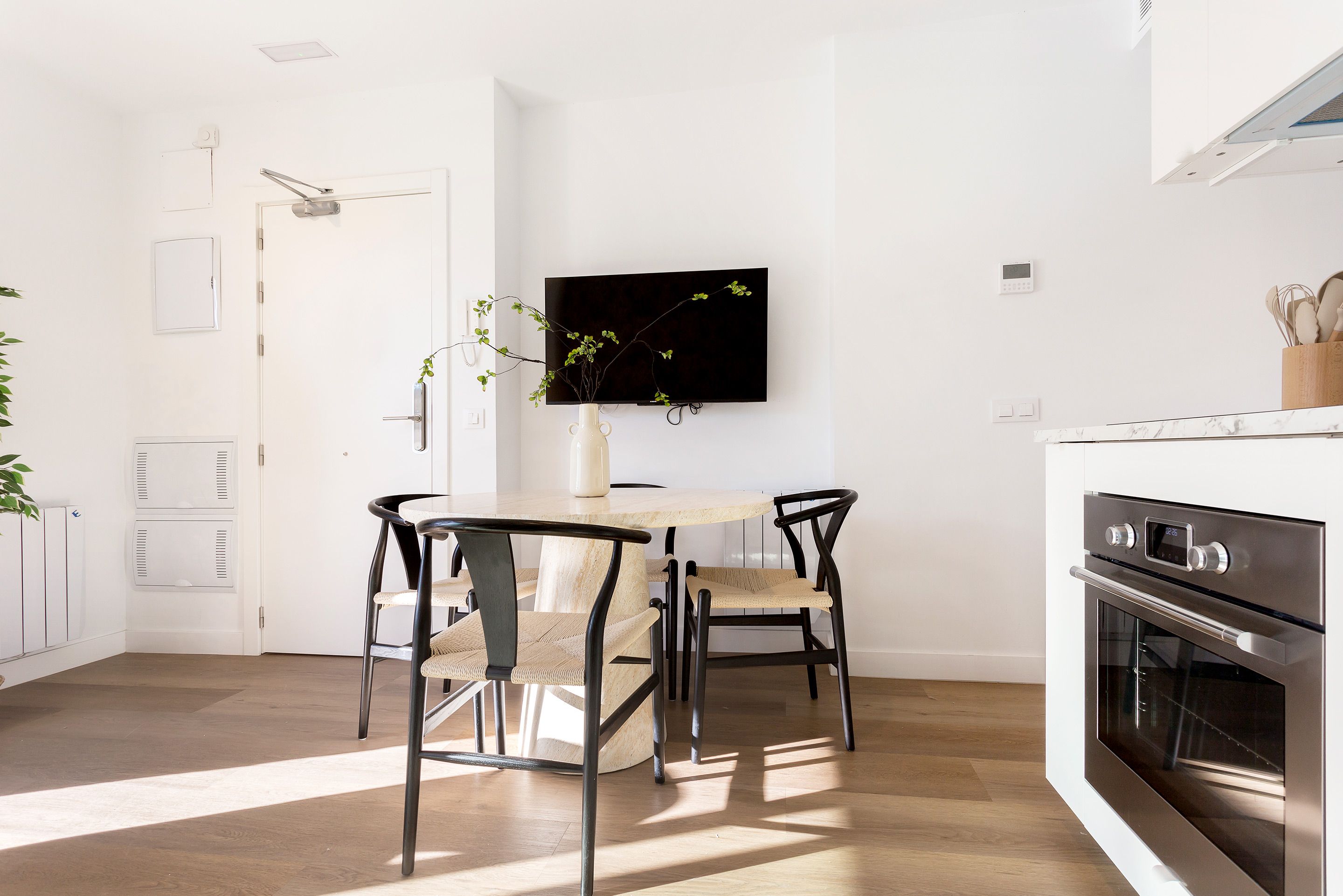 A modern kitchen with a dining area, a flat-screen TV mounted on the wall, and a built-in oven.