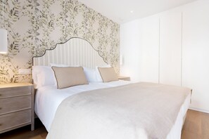 Ein Schlafzimmer mit einem Bett, Nachttischen, einer Kommode und einer Wand mit Blumenmuster.