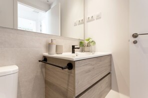 A modern bathroom with a white vanity, a mirror, a toilet, and a plant. - Genteel Home Zabaleta Terrace VI (Madrid)