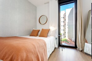 Ein Schlafzimmer mit einem Bett, einem runden Spiegel und Blick auf Gebäude durch eine Tür.