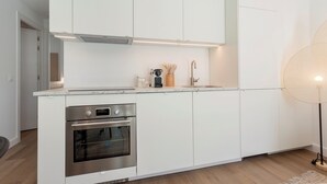 Et moderne køkken med hvide skabe, en indbygget ovn og en bordplade med kaffemaskine og redskaber.