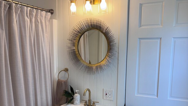 A bathroom with a white sink, a mirror with a sunburst frame, and a shower curtain. - Designed for You - Beautifully Renovated 2 Bedroom (Pawtucket)