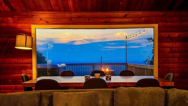 A cozy dining area with a table and chairs, a view of a balcony with a railing, and a warm interior with wooden walls. - Iconic Chalet: Sauna • Hot Tub • Fire Pit • Plunge (Shannondale)
