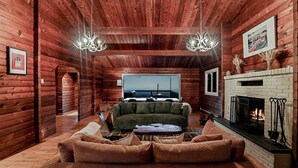 A log cabin interior with a fireplace, a green sofa, and a large window overlooking a body of water. - Iconic Chalet: Sauna • Hot Tub • Fire Pit • Plunge (Shannondale)