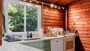 A kitchen with wooden walls, a window with a view of trees, a sink, and a stove. - Iconic Chalet: Sauna • Hot Tub • Fire Pit • Plunge (Shannondale)