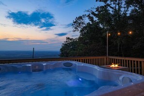 Un bain à remous doté d’un foyer, entouré d’une terrasse en bois et offrant une vue sur un plan d’eau.