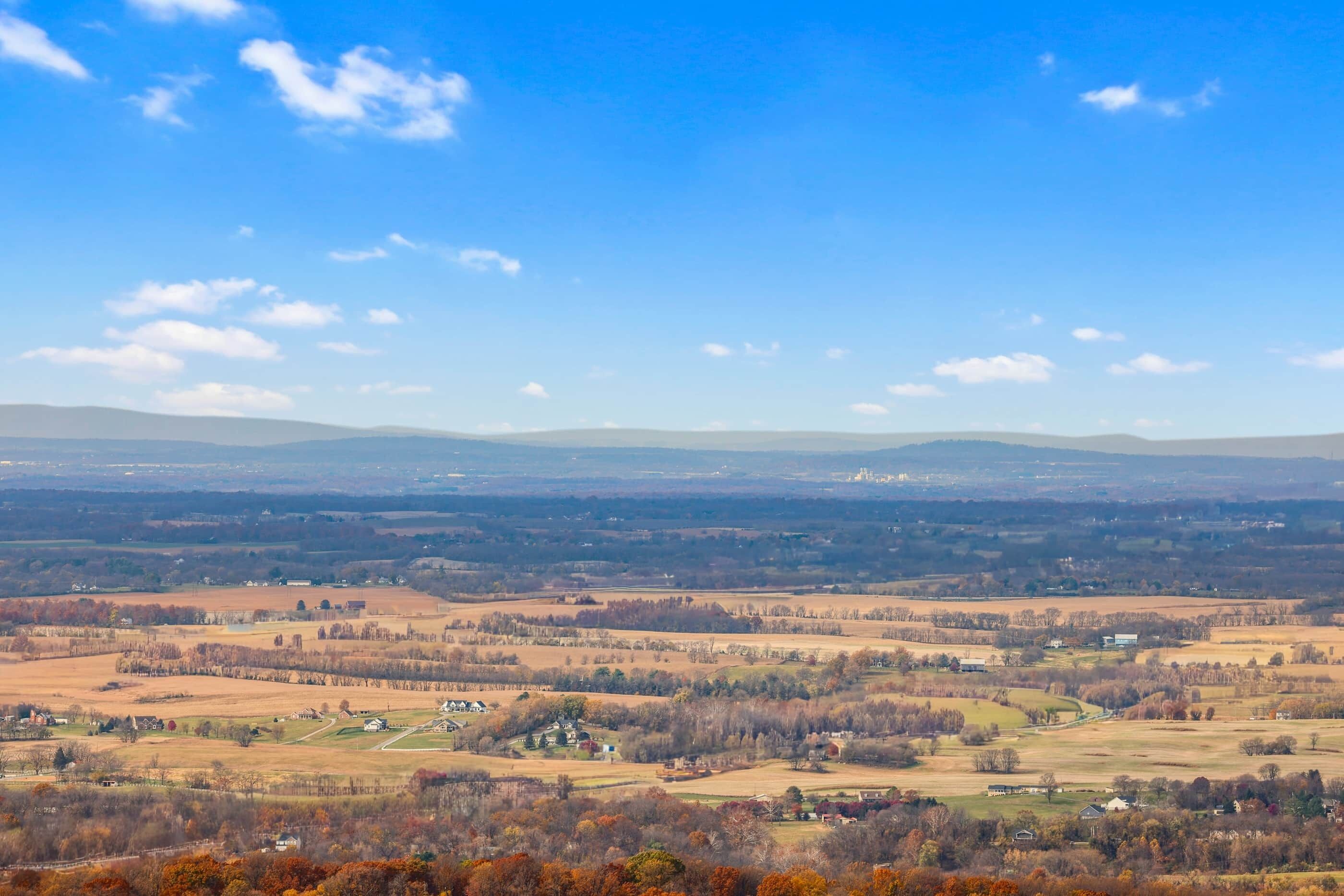 A panoramic view of a rural landscape with rolling hills, scattered houses, and a clear blue sky.