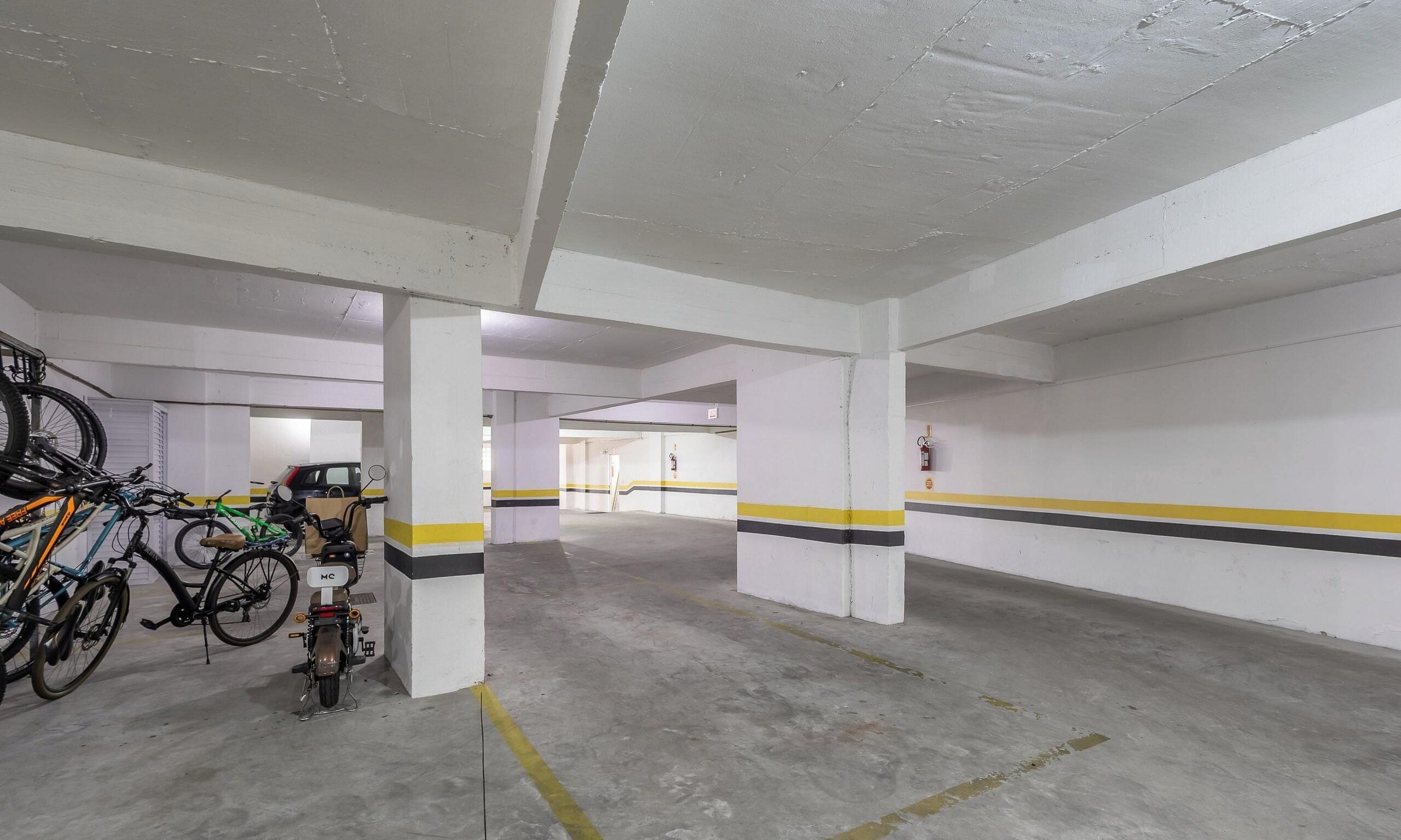A parking garage with concrete pillars, yellow and black stripes on the walls, and bicycles parked against the walls.