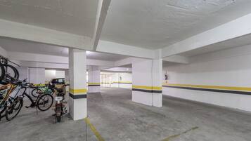 A parking garage with concrete pillars, yellow and black stripes on the walls, and bicycles parked against the walls.