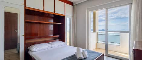 A bedroom with a bed, a wardrobe, a mirror, and a balcony with a view.