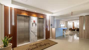 A modern lobby with two elevators, a reception desk, and a waiting area with seating.