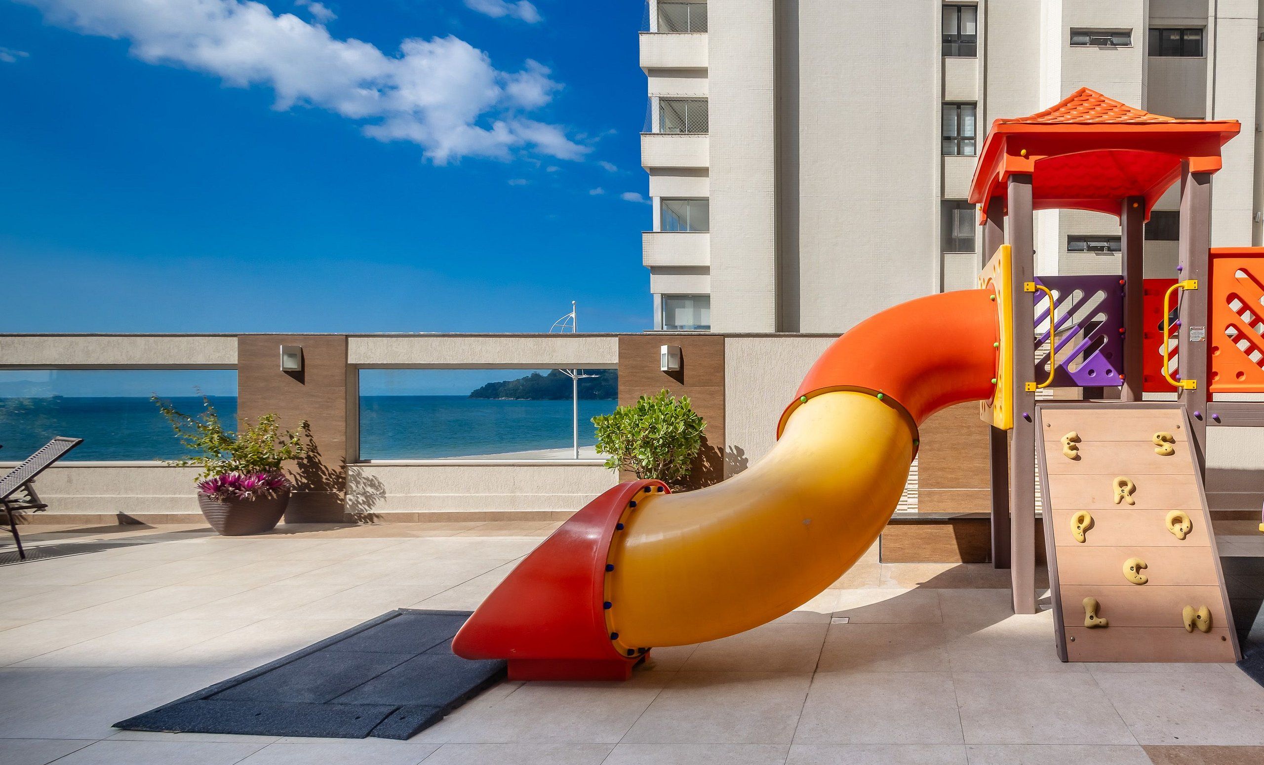 Zona de juegos infantiles con tobogán, pared de escalar y vista al mar.