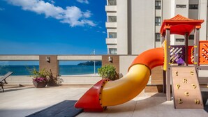 A children's play area with a slide, a climbing wall, and a view of the sea. - Your Stay by the Seaside in the Best Location of BC - Cets (Balneário Camboriú)