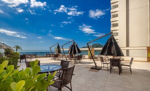 An outdoor seating area with tables and chairs, umbrellas, and a view of the sea. - Your Stay by the Seaside in the Best Location of BC - Cets (Balneário Camboriú)