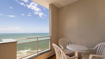 A balcony with a view of the ocean, a small round table with chairs, and a tiled wall.