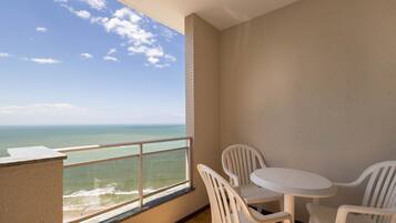 A balcony with a view of the ocean, a small round table with chairs, and a tiled wall.