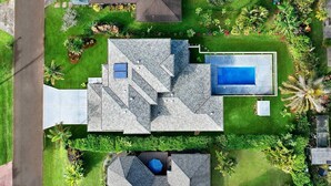 Una casa moderna con piscina, rodeada de césped cuidado y diversas plantas.