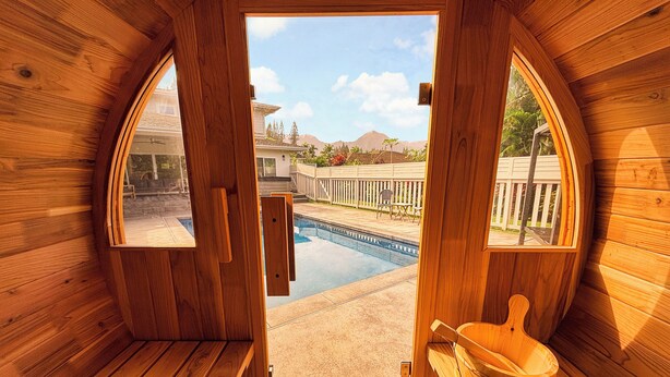 Una sauna con paredes de madera, un banco de madera, un balde de madera y vistas a una piscina y montañas.