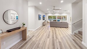 Un pasillo amplio con piso de madera, un espejo redondo, una mesa consola con un teclado y una escalera que conduce a un balcón con vistas.