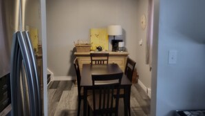 Une cuisine compacte comprenant une table à manger, des chaises, un réfrigérateur, une lampe et une horloge murale.