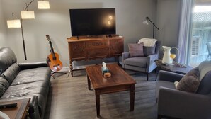 Un salon avec un canapé en cuir, une table basse en bois, un téléviseur et une guitare.