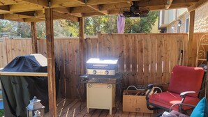 Un patio extérieur couvert, équipé d’un barbecue, d’un gril, d’une chaise rouge et d’une table sur laquelle est posé un panneau indiquant « Bienvenue ».