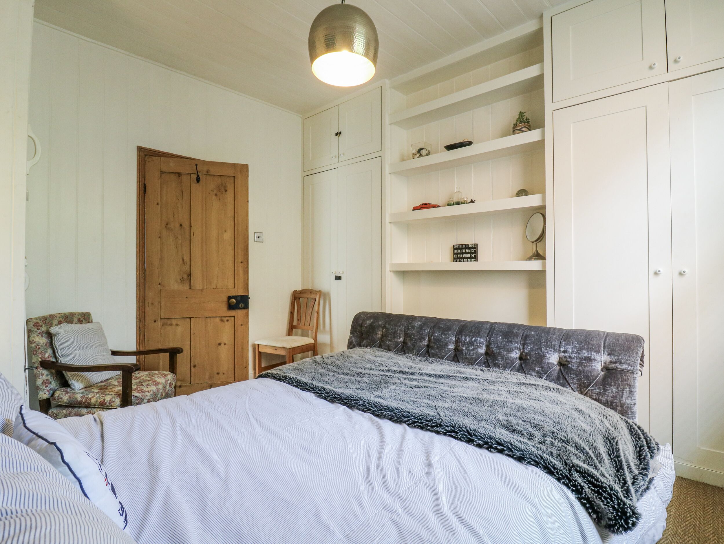 Une chambre à coucher avec un lit, une porte en bois, une chaise et une étagère contenant divers objets.