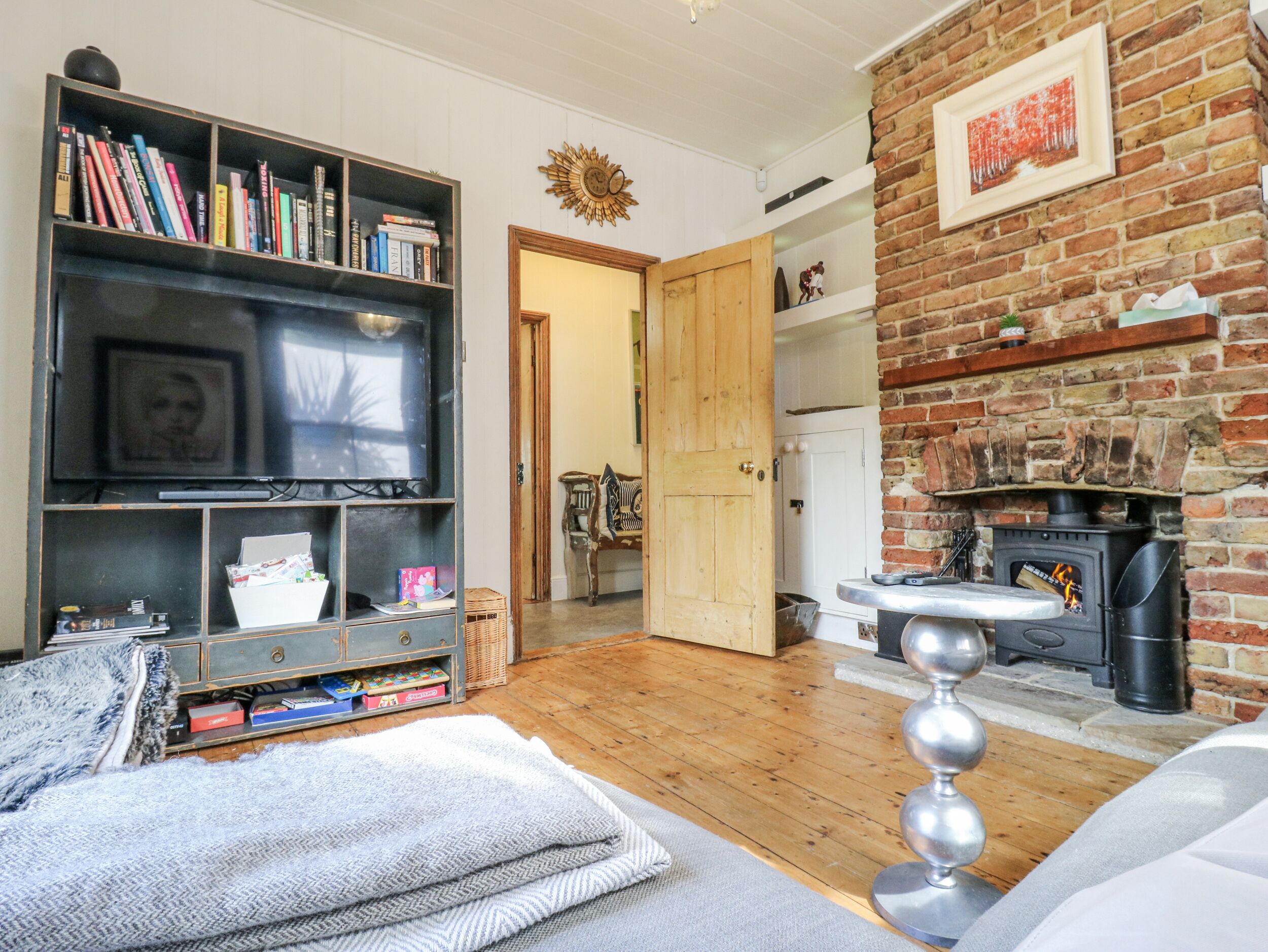 Ein gemütliches Wohnzimmer mit Kamin, Bücherregal, Fernseher und einer Tür zu einem anderen Raum.