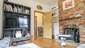 Una sala de estar acogedora con chimenea, una estantería, un televisor y una puerta que da a otra habitación.