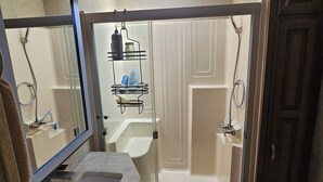 A bathroom with a large mirror, a sink, a shower with glass doors, and a ceiling light. - Camper on peaceful gated property. (North Fort Myers)