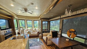 A modern kitchen with a central island, a dining area with a wooden table, and a seating area with sofas. - Camper on peaceful gated property. (North Fort Myers)