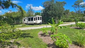 A recreational vehicle (RV) parked in a grassy area with trees and a clear sky. - Camper on peaceful gated property. (North Fort Myers)