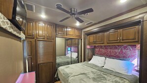 A compact RV bedroom with two beds, wooden cabinets, a ceiling fan, and a TV mounted on the wall. - Camper on peaceful gated property. (North Fort Myers)