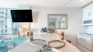 A modern kitchen with a large island, a flat-screen TV, a microwave, and a view of a high-rise building.