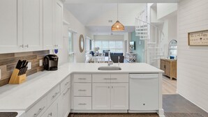 Una cocina moderna con armarios blancos, una isla central y un comedor al fondo.