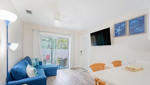 Un salon moderne avec un canapé bleu, des fauteuils verts, une table à manger blanche et un téléviseur fixé au mur.