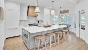 Une cuisine spacieuse dotée d’un grand îlot central, de tabourets en bois et de luminaires suspendus.
