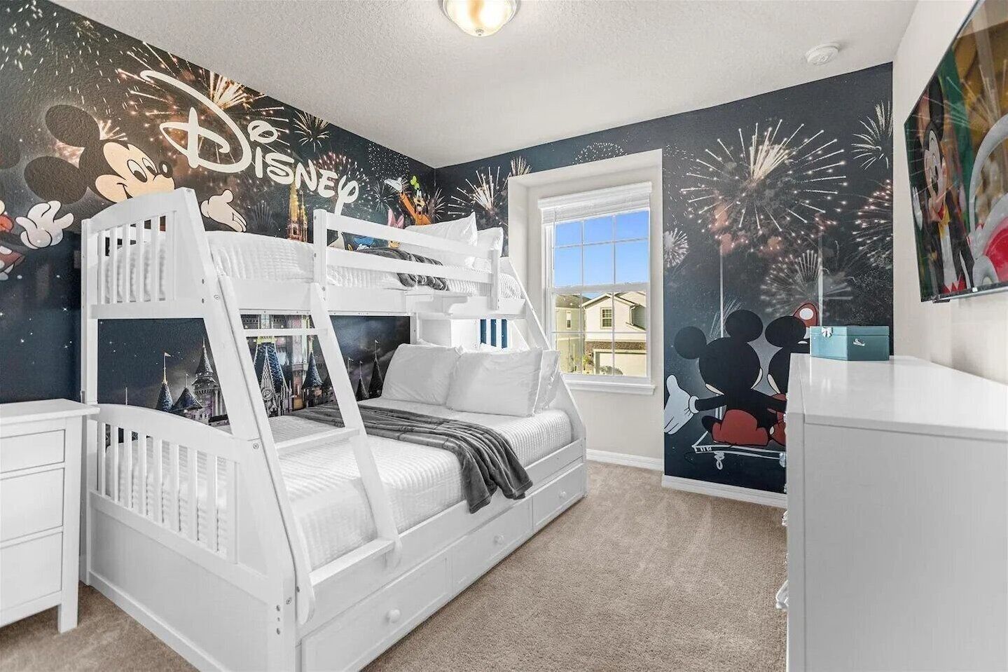 A child's bedroom with a bunk bed, Disney-themed wallpaper, and a window with a view of houses.
