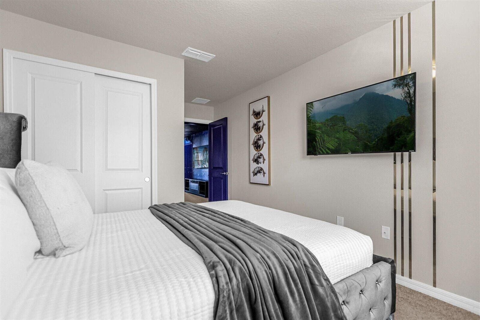 A bedroom with a bed, a TV mounted on the wall, and a door leading to another room.