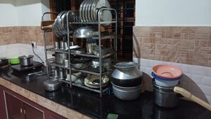 A kitchen with a metal dish rack holding various pots and pans. There is a green container on the counter, and a pink bowl with a lid.