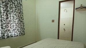 A room with a bed, a patterned curtain, a tiled wall, and a door with a towel hanging on it.