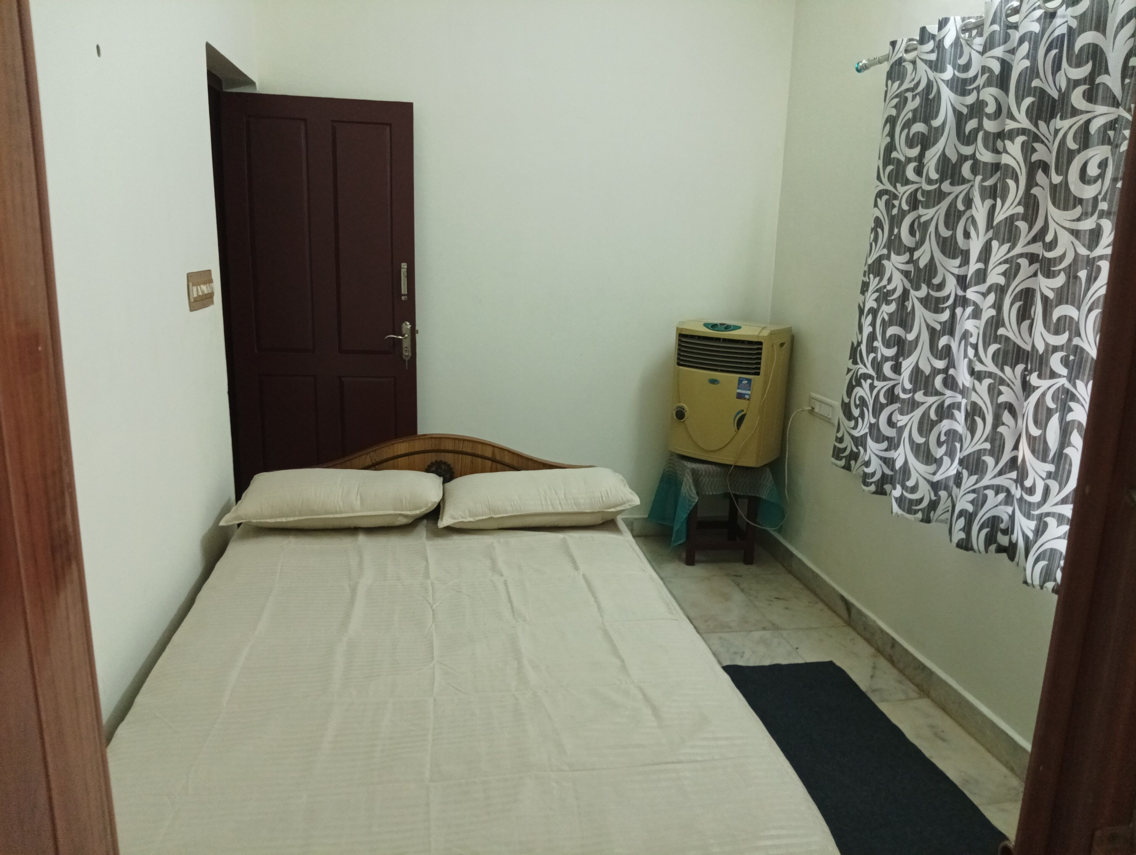 A small, simple room with a bed, a door, a heater, and a curtain.