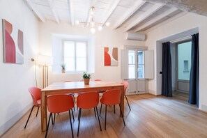 Un coin repas avec une table en bois et des chaises orange, une plante en pot et des œuvres d’art abstraites accrochées au mur.
